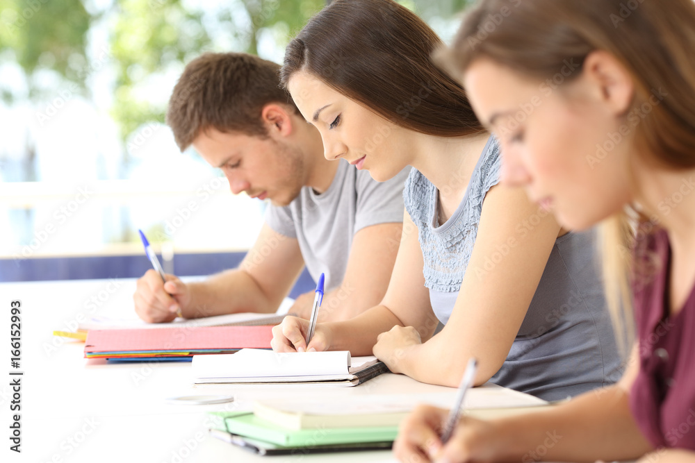 Three students taking notes during a class Three students taking notes during a class