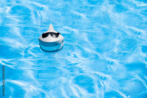 A plastic pool shark chlorinator is wearing sunglasses and a big smile as it does its job in the pool  photo