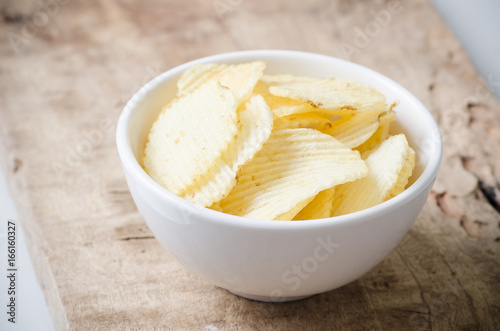 Potato chips in a bowl on wooden background