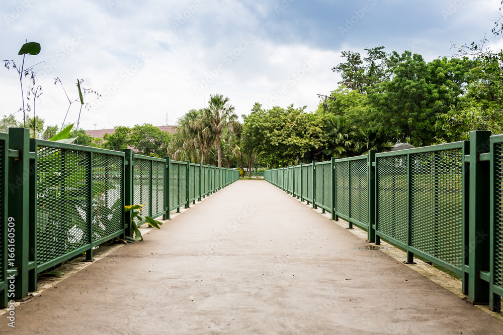 Concrete bicycle bridge with green fence in park