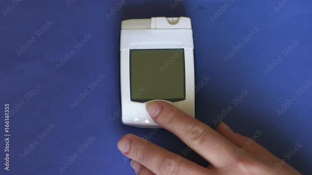 Close-up of the girl turns glucometer on a blue background. Result of the measurement of blood sugar on the screen of the meter. 7 mmol. Close-up of the girl turns glucometer on a blue background. Result of the measurement of blood sugar on the screen of the meter. 7 mmol.