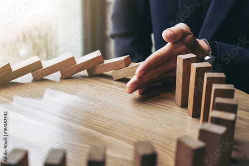 Foto Close up of businessman hand Stopping Falling wooden Dominoes effect from contin