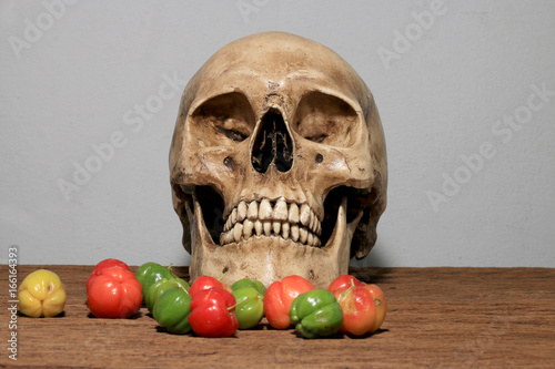 Still life photography with human skull and fresh Cherries at harvest time on wooden table with wall background. photo