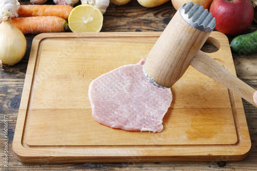 Meat mallet and beaten piece of veal on cutting board photo