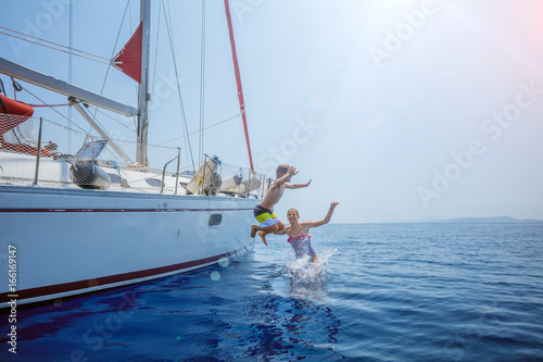 Boy with his sister jump of sailing yacht on summer cruise. Travel adventure, yachting with child © Max Topchii