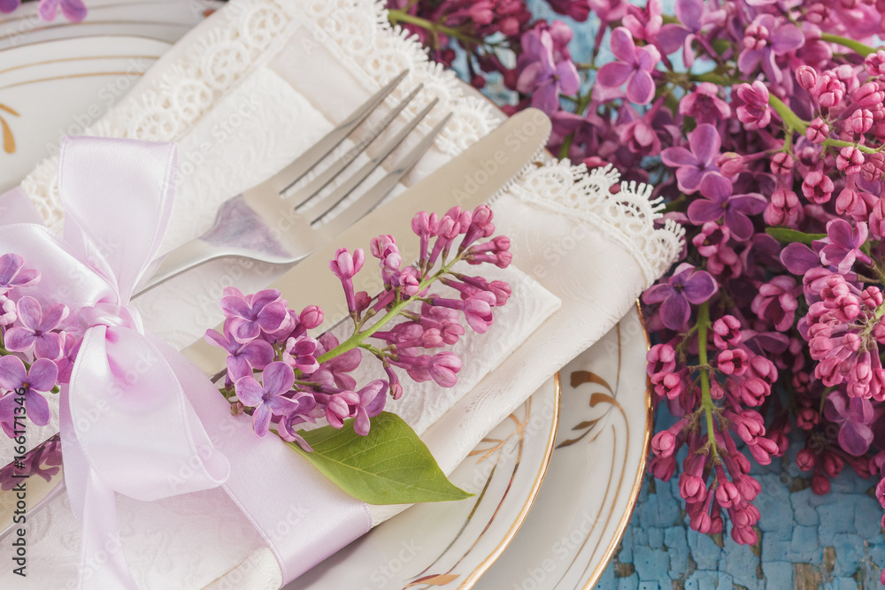 Tableware and silverware with bunches of violet lilac on the wooden background Tableware and silverware with bunches of violet lilac on the wooden background
