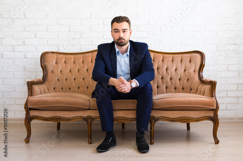 business, richness and success concept - handsome bearded man sitting on vintage sofa