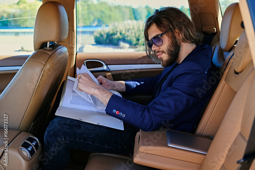 A man sits in a car and working with paper documents.