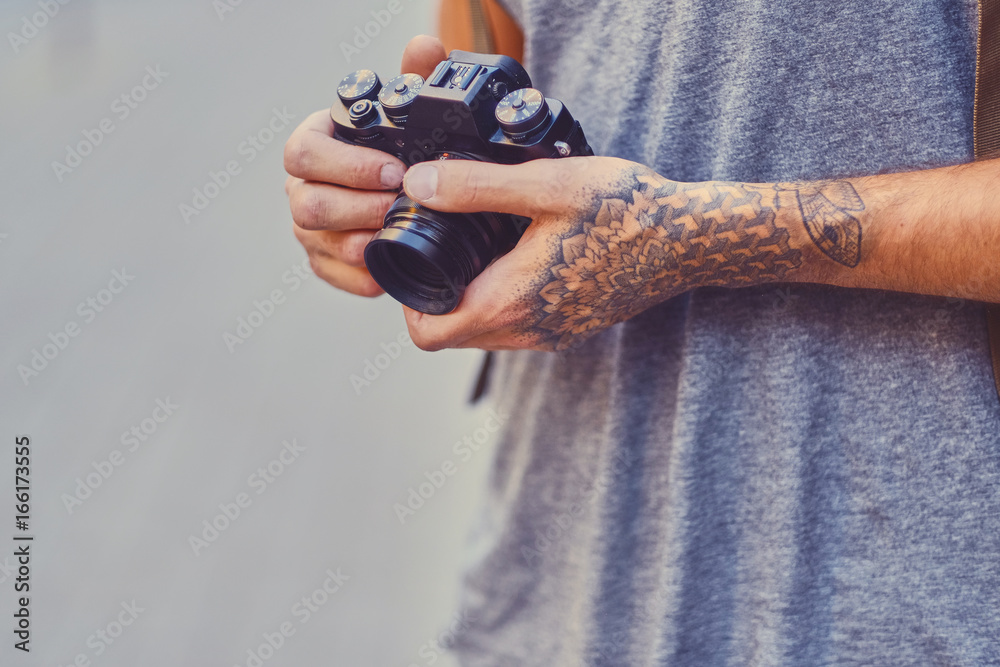 Fototapeta premium A man holds a compact film camera with tattooed arms.