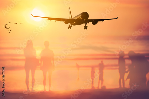 Airplane flying over blur people relax on tropical sunset beach with bokeh sun light wave abstract background.