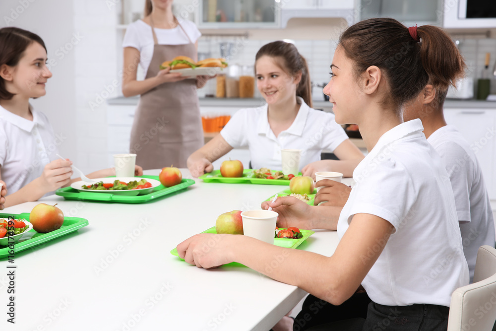 Children sitting at table in school cafeteria while eating lunch Children sitting at table in school cafeteria while eating lunch