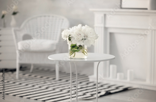 Glass vase with beautiful peonies on table in room