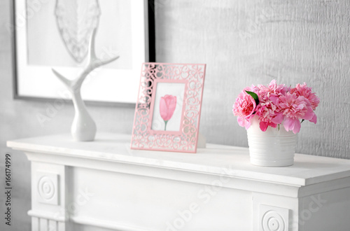 Interior of light room with beautiful peonies in vase on mantelpiece
