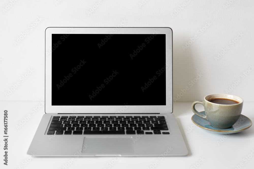 Modern technology, communication, electronic devices, gadgets, work and communication. Mock up of workplace: white table with coffee cup and generic notebook computer with blank copyspace screen Modern technology, communication, electronic devices, gadgets, work and communication. Mock up of workplace: white table with coffee cup and generic notebook computer with blank copyspace screen