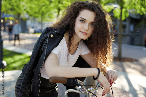 Beautiful high school student girl with pretty face and bushy hairstyle enjoying summer vacations in town, riding retro bike in the morning. People, urban active lifestyle, transportation and leisure