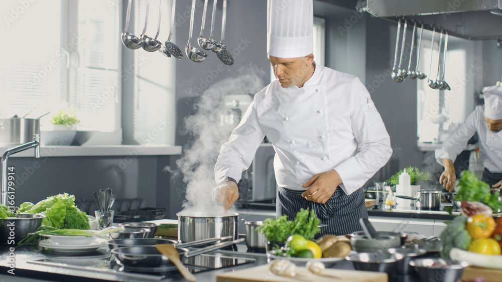 Famous Chef of a Big Restaurant Prepares Dishes with His Help of Cooks. Modern Kitchen is Made of Stainless Steel and Full of Cooking Ingredients. Famous Chef of a Big Restaurant Prepares Dishes with His Help of Cooks. Modern Kitchen is Made of Stainless Steel and Full of Cooking Ingredients.