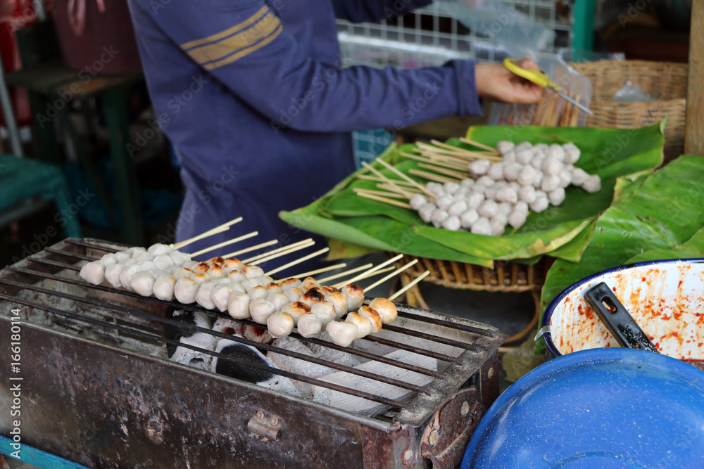 Pork ball with wood stick grilling on the metal grill grate in the stove, raw Pork ball prepare on the banana leaf. Thai lifestyle food in the market.