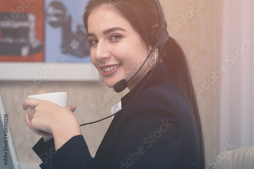 Young beautiful girl working at a laptop in a small medium enterprise. She is operating the phones and computer