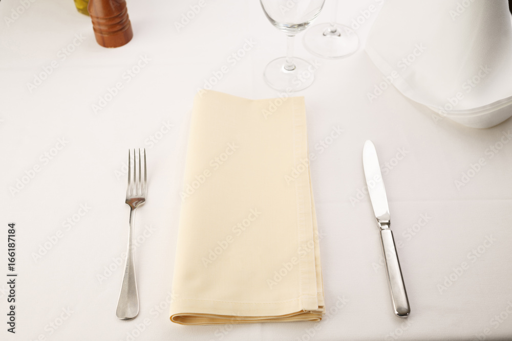 Fork and table knife with napkin arranged in elegant setting, Wineglass in the background, Selective focus with soft light