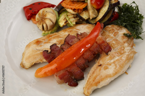 Chicken with bacon and grilled vegetables arranged on a plate, Traditional dish in elegant setting, Selective focus with soft light