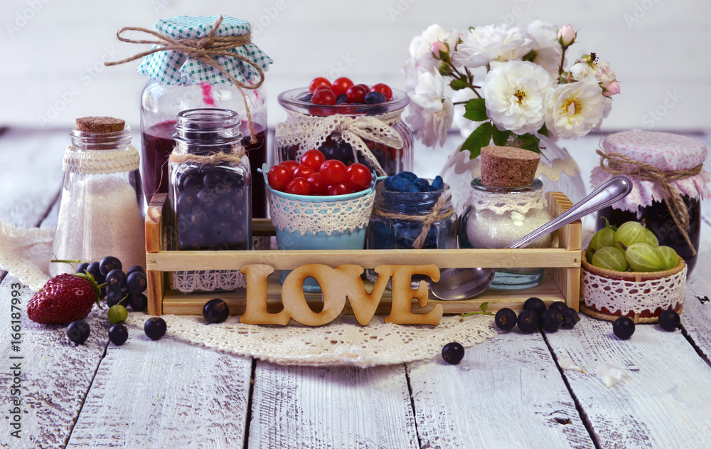 Fresh berry and homemade jam in bottles decorated with cloth, ribbon and flowers