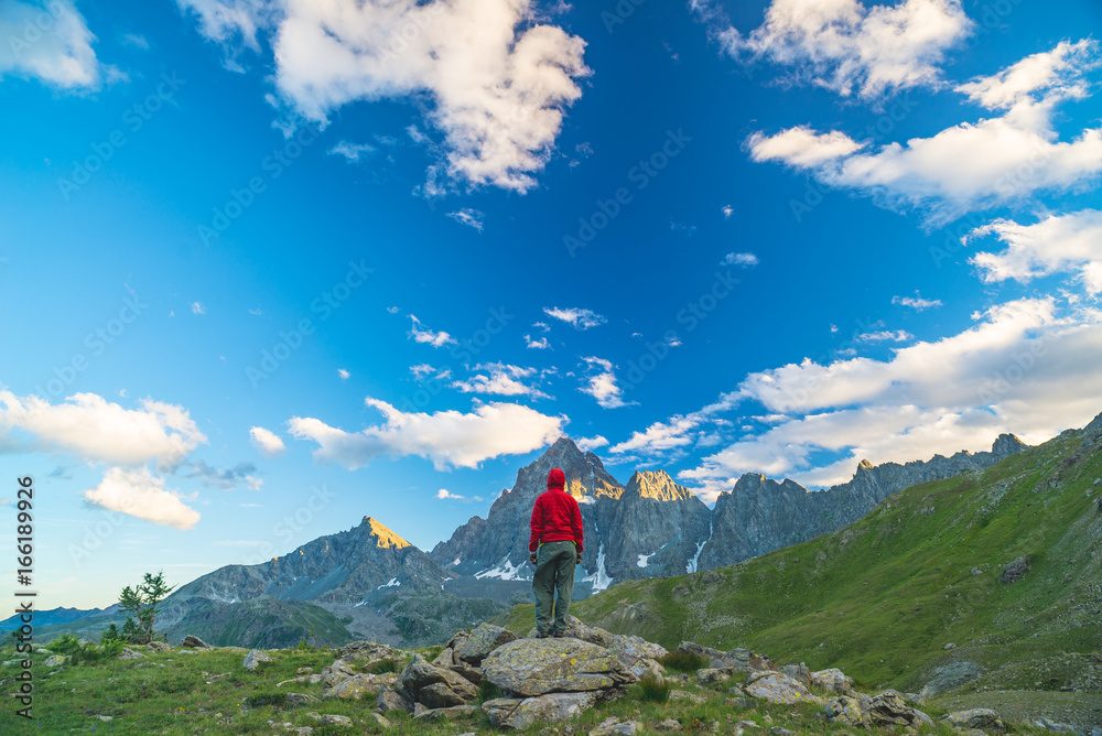 One person looking at the majestic view of glowing mountain peaks at sunset high up on the Alps. Rear wide angle view, toned and filtered image.