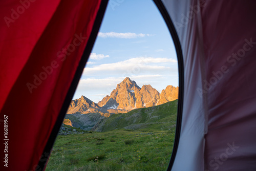 Looking out the mountain landscape at sunrise from interior of camping tent. Adventure traveling on the majestic European Alps, summer outdoor activities.