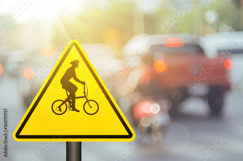 Bicycle warning sign on blur traffic road with colorful bokeh light abstract background.