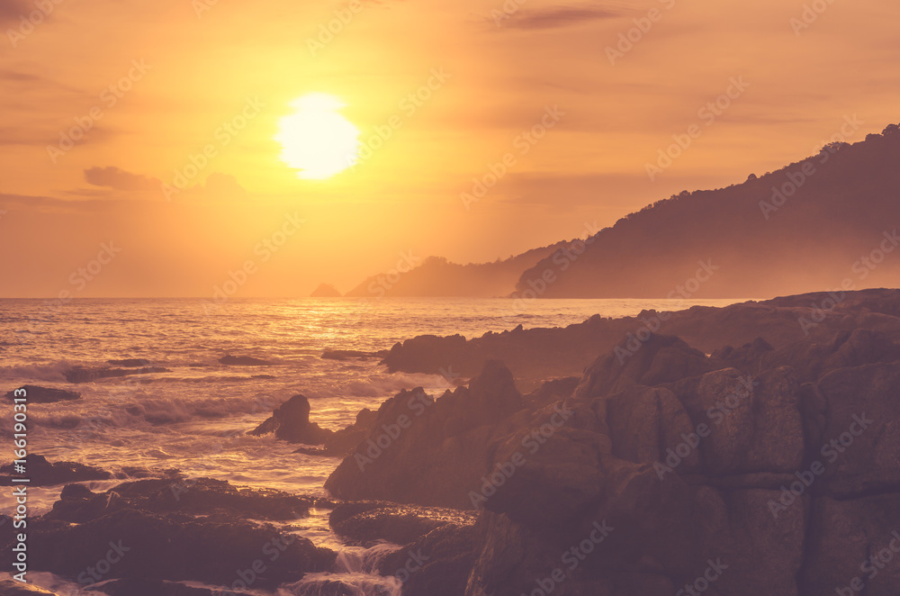 Obraz premium Wave splash on rock in sunset beach background. Copy space of outdoor summer vacation and business travel adventure concept.