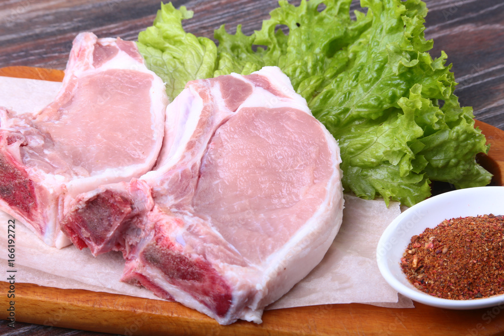 Raw pork steak with spices Leaves lettuce on wooden cutting board. Ready for cooking. Raw pork steak with spices Leaves lettuce on wooden cutting board. Ready for cooking.