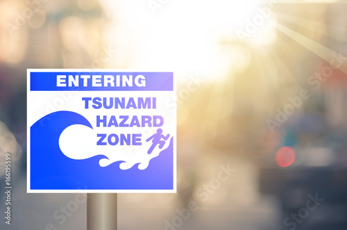 Tsunami hazard zone warning sign on blur traffic road with colorful bokeh light abstract background.