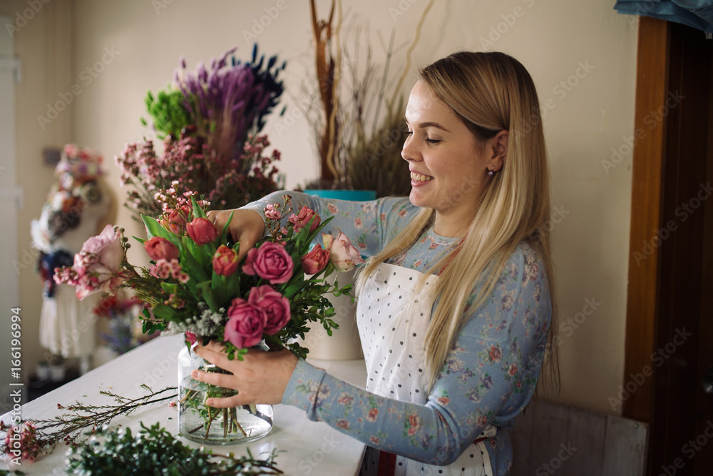 woman florist making bouquet of flowers indoor. Female florist preparing bouquet with roses, tulip in flower shop