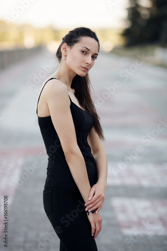 Fashion lifestyle portrait young brunette pretty woman posing in the city quay summer sunset evening showing street fashion ideas