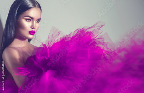 Gorgeous brunette model woman in purple dress posing in studio