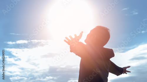 Freedom and feel good concept. Copy space of silhouette man rising hands on sunset sky background.