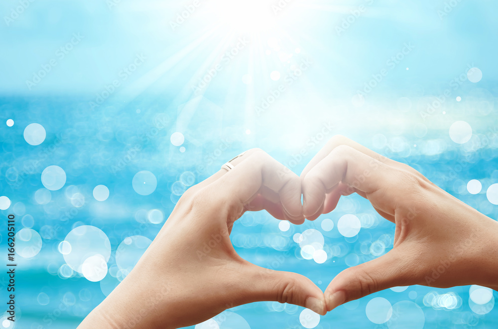 Female hands heart shape on nature bokeh sun light flare wave and blur tropical beach abstract background. Female hands heart shape on nature bokeh sun light flare wave and blur tropical beach abstract background.