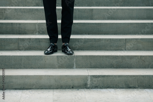 Men fashion, movie star concept. Standing on stone stairs man wearing black pants and patent leather shoes. Iconic classic Hollywood style. Outdoor shot