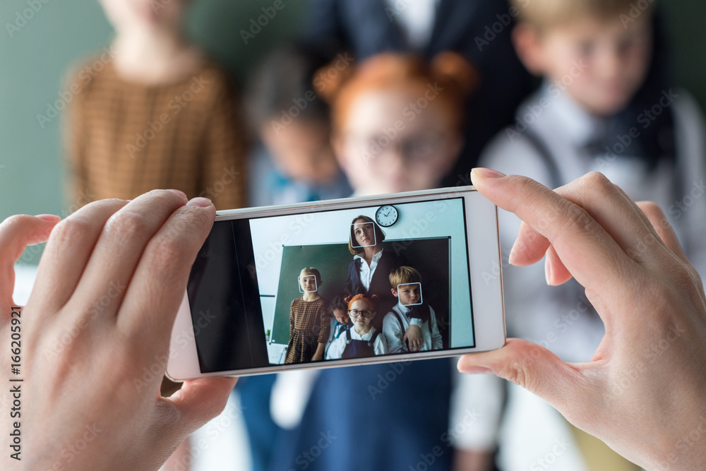 close-up view of young female teacher and cute little students photographing with smartphone - obrazy, fototapety, plakaty 