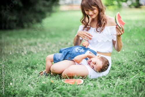 Mother and young son played on grass. Happy family walks in the Park. Mom and young son eating watermelon. Picnic. Summer.