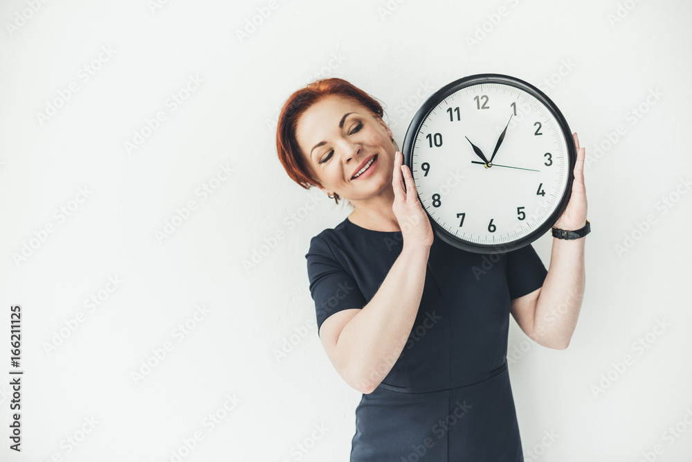 happy mature woman holding clock on white wall background happy mature woman holding clock on white wall background