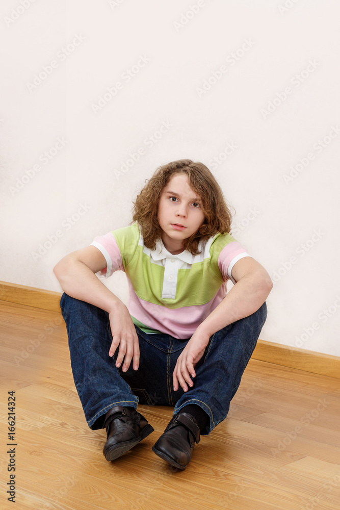 The eleven-year-old boy with long hair sits on a floor and looks in a lens The eleven-year-old boy with long hair sits on a floor and looks in a lens