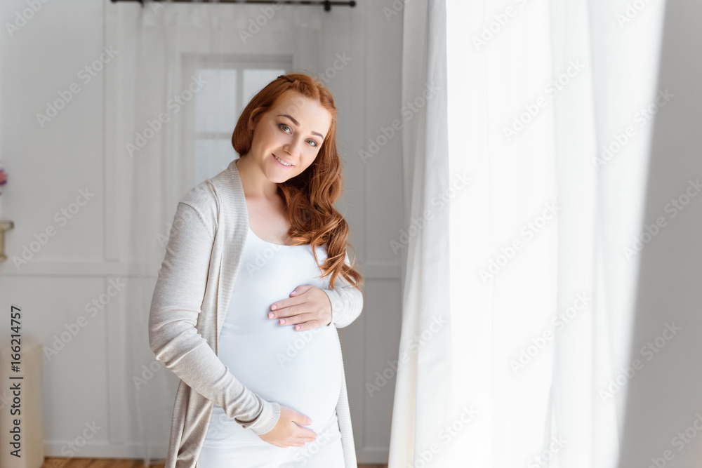 smiling beautiful pregnant woman touching her belly and looking at camera at home smiling beautiful pregnant woman touching her belly and looking at camera at home
