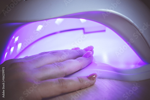 Professional ultraviolet nail manicure lamp drying shell gel polishing on woman's hand in a beauty salon photo