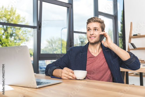 portrait of young businessman talking on smartphone at workplace in office