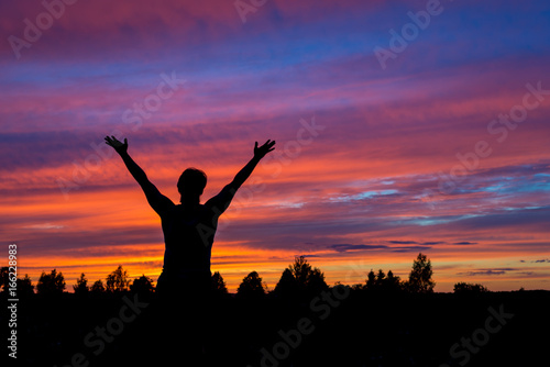 Man with hands up silhouette with colorful sunset