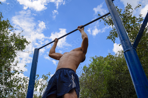 The man pulls himself up on the bar. Playing sports in the fresh air. Horizontal bar.