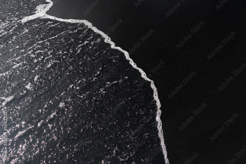 Fototapeta white ocean foam on black sand volcanic texture