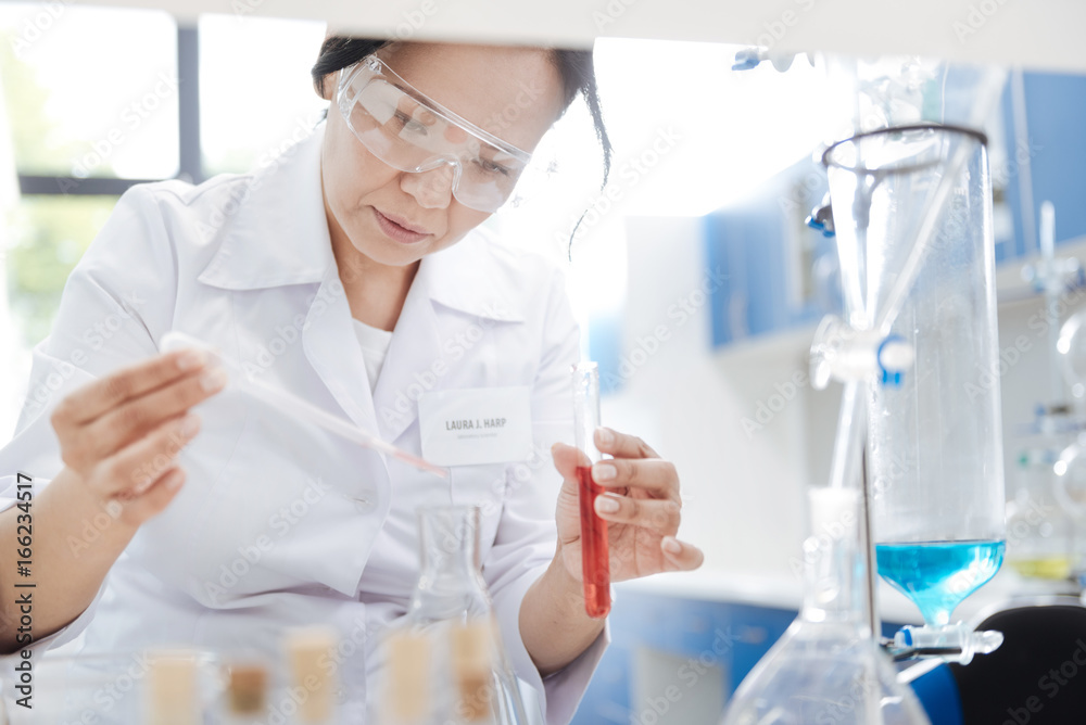 Fototapeta premium Nice smart woman putting chemical reagent into a flask