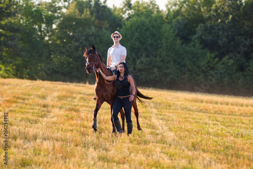 Woman and young man enjoy in nature riding a horse