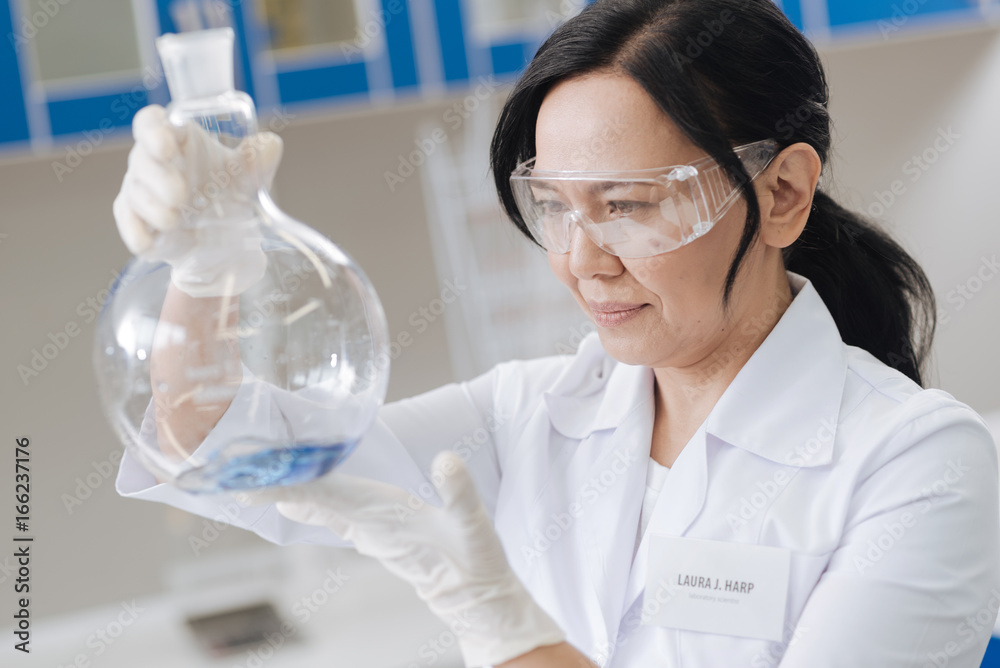 Cheerful positive chemist holding a flask with liquid Cheerful positive chemist holding a flask with liquid